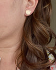 Model wearing handmade jeweler's brass hydrangea petal impression stud earrings, nature inspired botanical jewelry handcrafted in Vermont