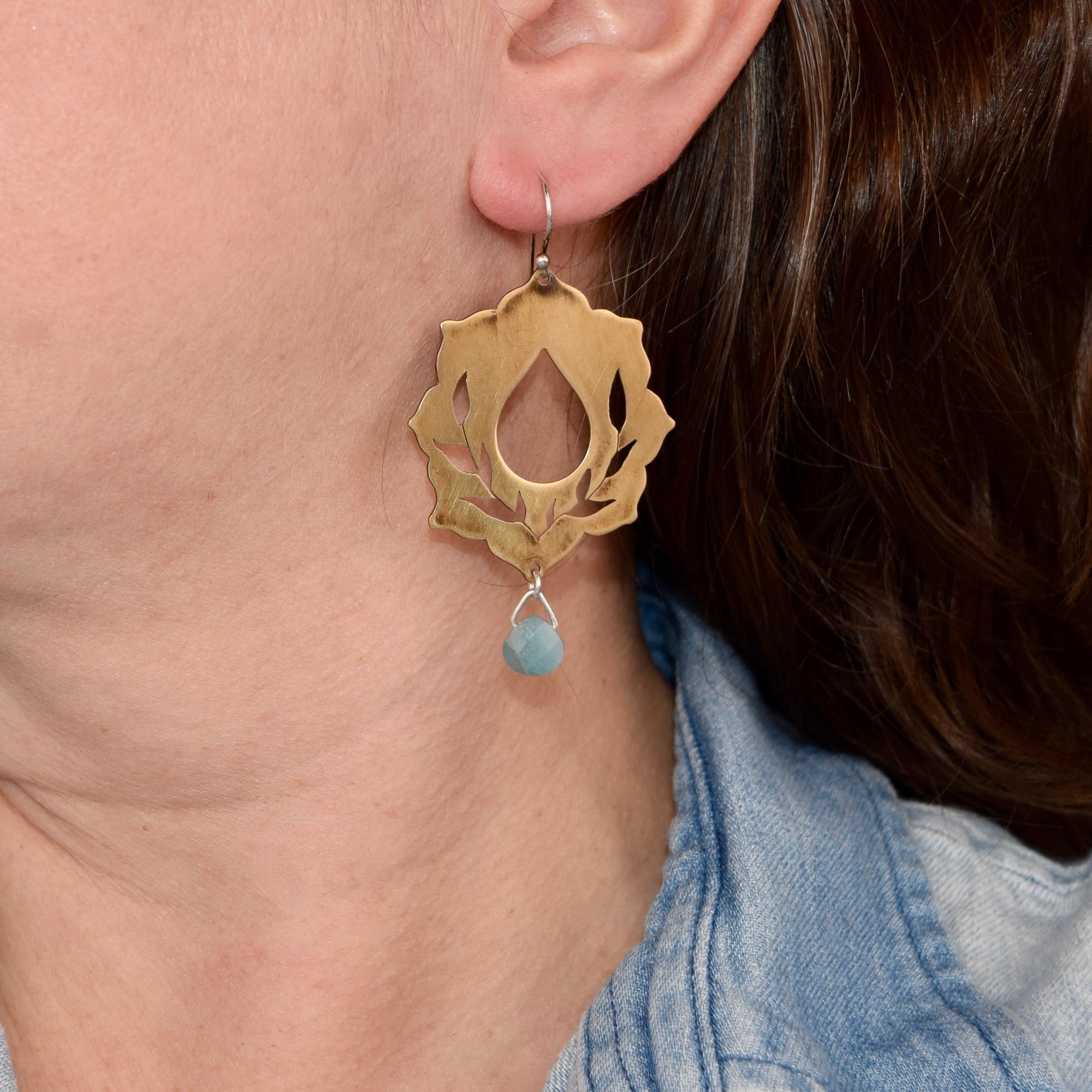 Brassearring with a blue gemstone worn by a person with a denim jacket.