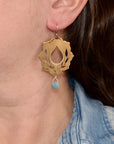 Brassearring with a blue gemstone worn by a person with a denim jacket.