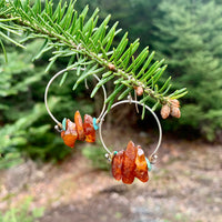 Handmade sterling silver hoop earrings with genuine raw amber and turquoise nuggets and brass wire wrapping displayed on pine tree branch, artisan gemstone jewelry crafted in Vermont