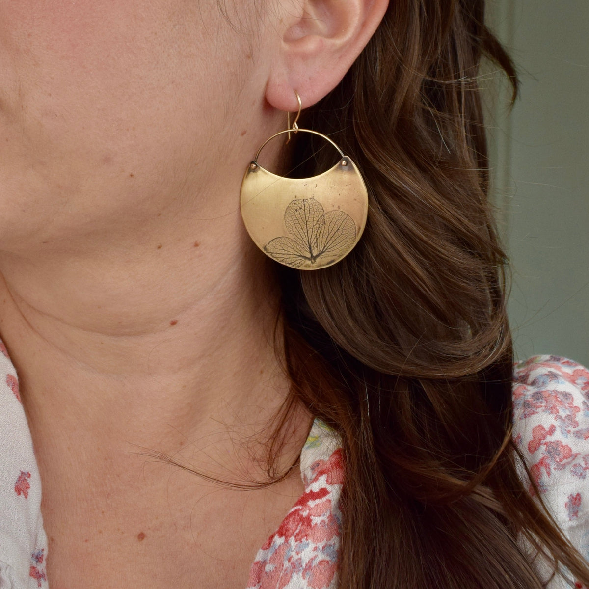 Model wearing large handmade brass hydrangea crescent dangle earrings, statement botanical nature jewelry crafted in Vermont