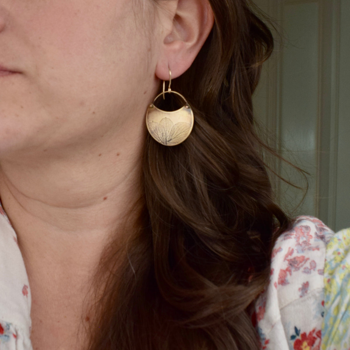 Model wearing medium handmade brass hydrangea crescent dangle earrings, rustic botanical jewelry handcrafted in Vermont
