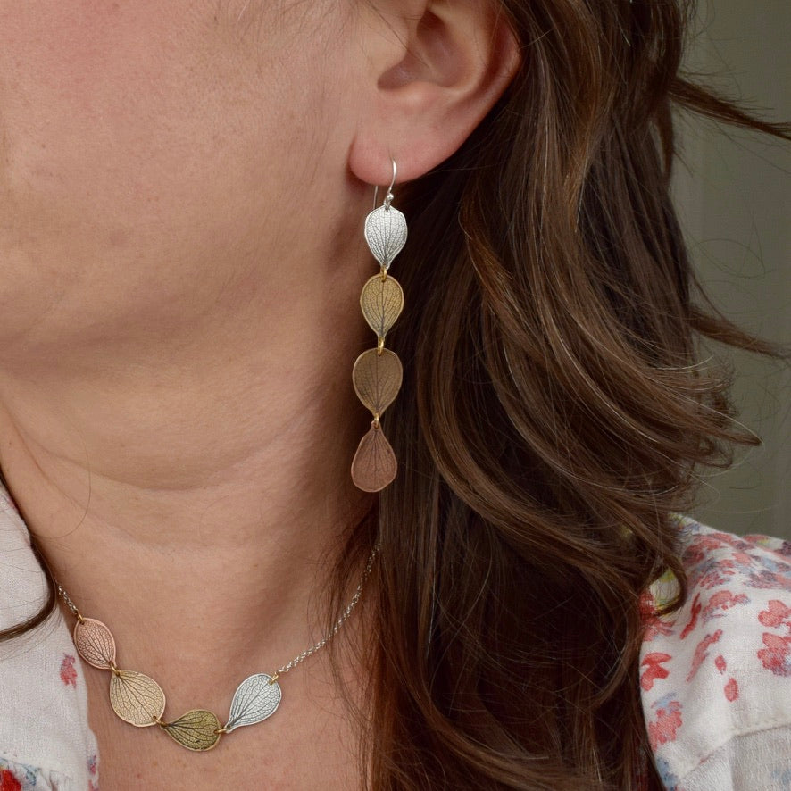 Model wearing handmade hydrangea petal ombré drop earrings in sterling silver brass bronze and copper, artisan botanical jewelry crafted in Vermont
