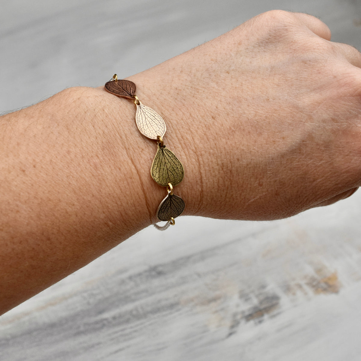Model wearing handmade hydrangea petal ombré bracelet in sterling silver brass bronze and copper, artisan botanical nature jewelry crafted in Vermont