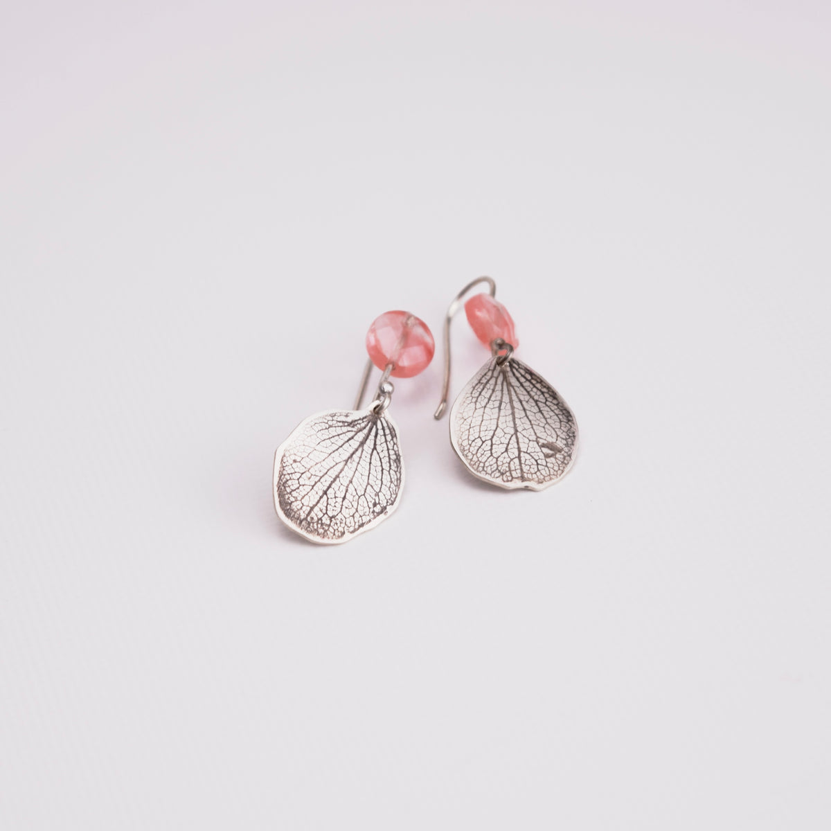 Overhead view of handmade sterling silver hydrangea petal and rose quartz dangle earrings, delicate botanical gemstone jewelry handcrafted in Vermont