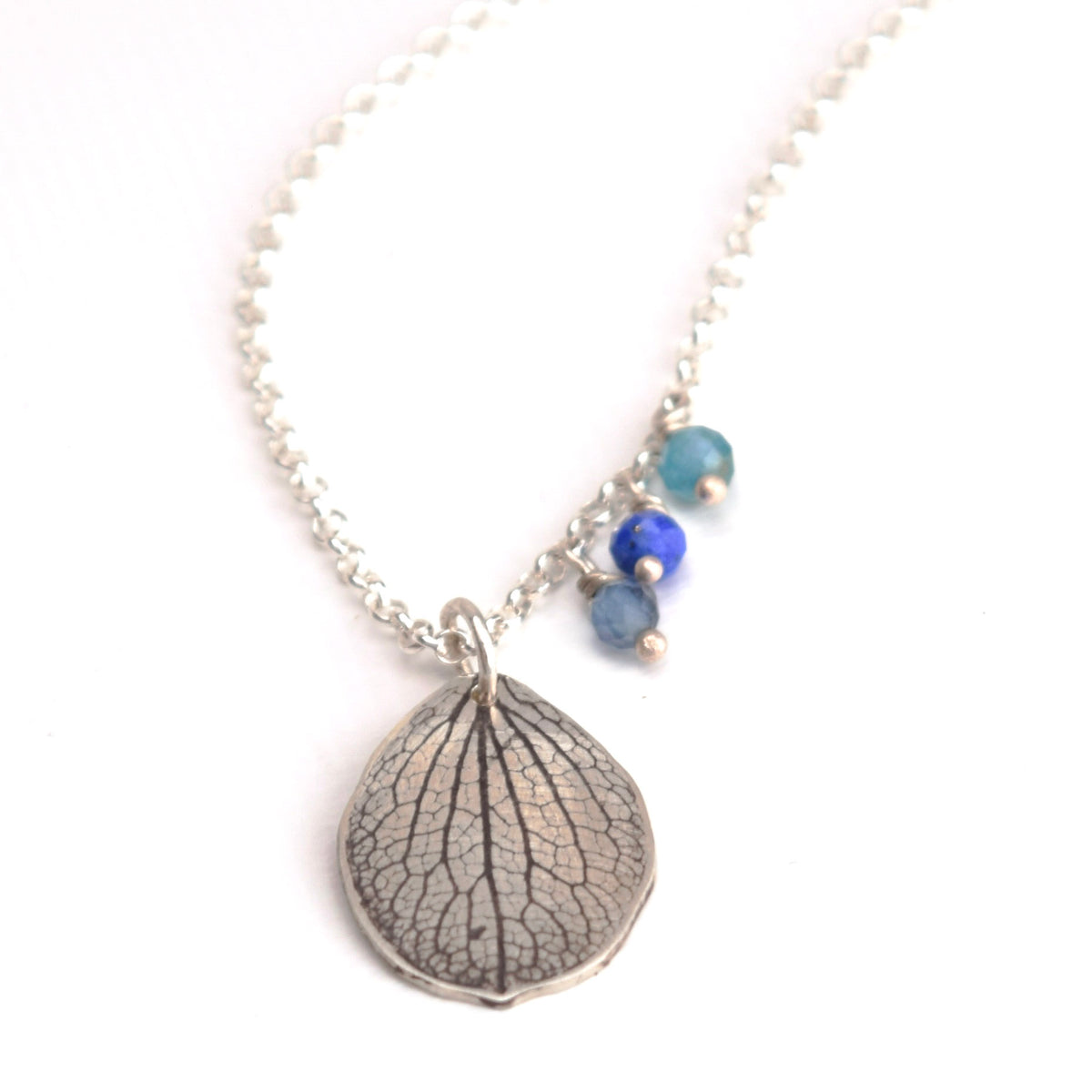 Overhead view of handmade sterling silver hydrangea petal necklaces with aquamarine, lapis lazuli and teal apatite gemstone charms, botanical gemstone jewelry crafted in Vermont