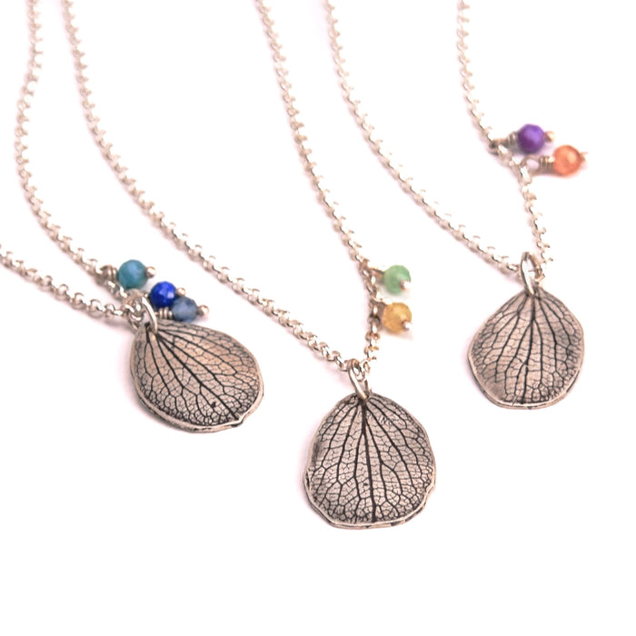 Overhead view of three handmade sterling silver hydrangea mother petal necklaces with various gemstone charm combinations, customizable botanical jewelry crafted in Vermont