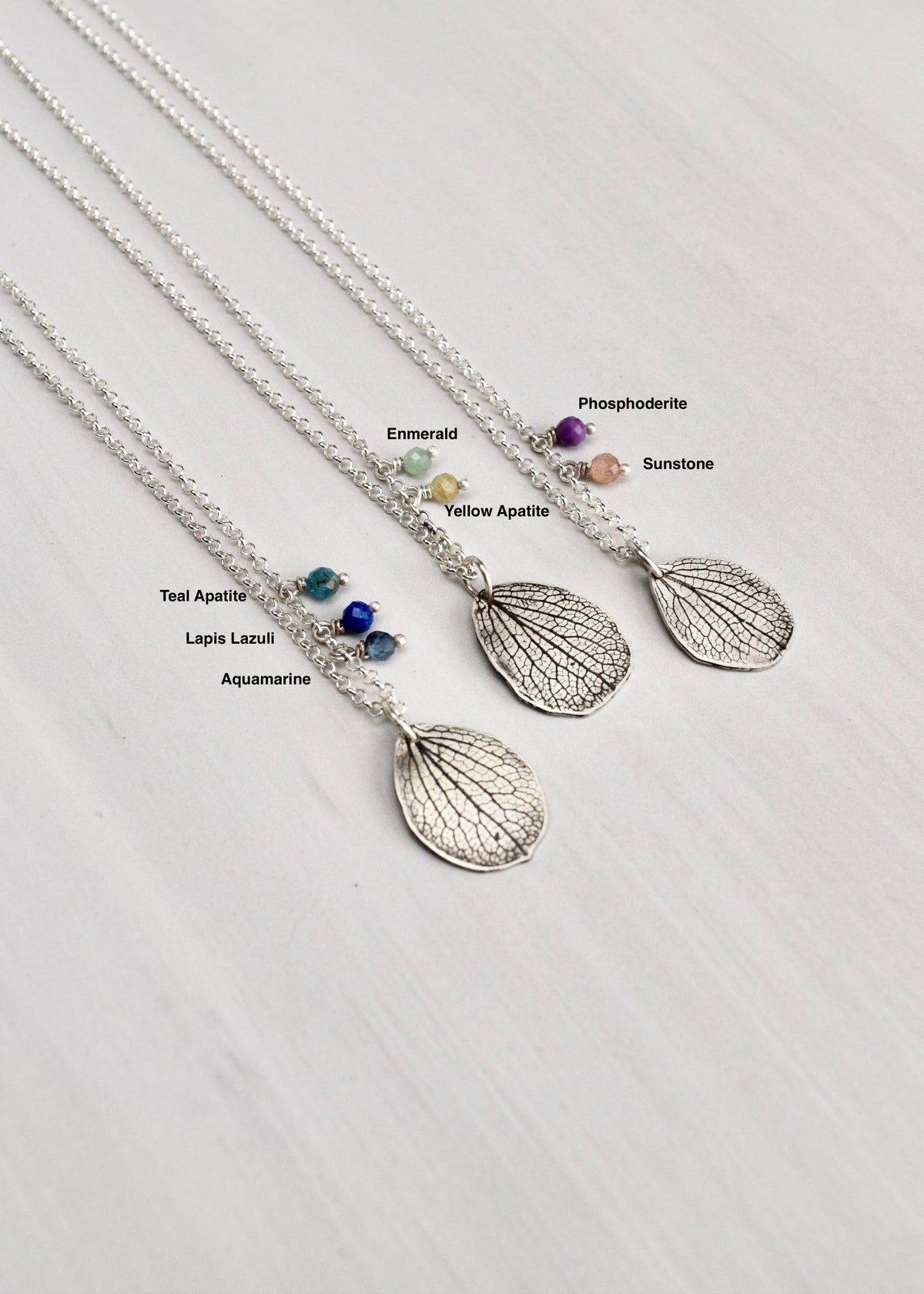 Overhead view of handmade sterling silver hydrangea mother petal necklaces showing available gemstone options including aquamarine, lapis lazuli, teal apatite, yellow apatite, emerald, sunstone and phosphosiderite