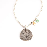 Overhead view of handmade sterling silver hydrangea petal necklace with yellow apatite and emerald gemstone charms, customizable nature jewelry crafted in Vermont