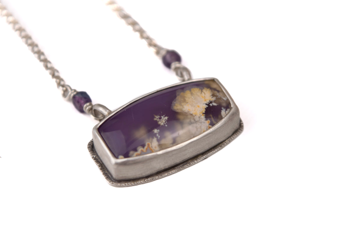 Three-quarter view of handcrafted purple plume agate pendant in sterling silver, fluorite bead bail detail, one-of-a-kind handmade necklace