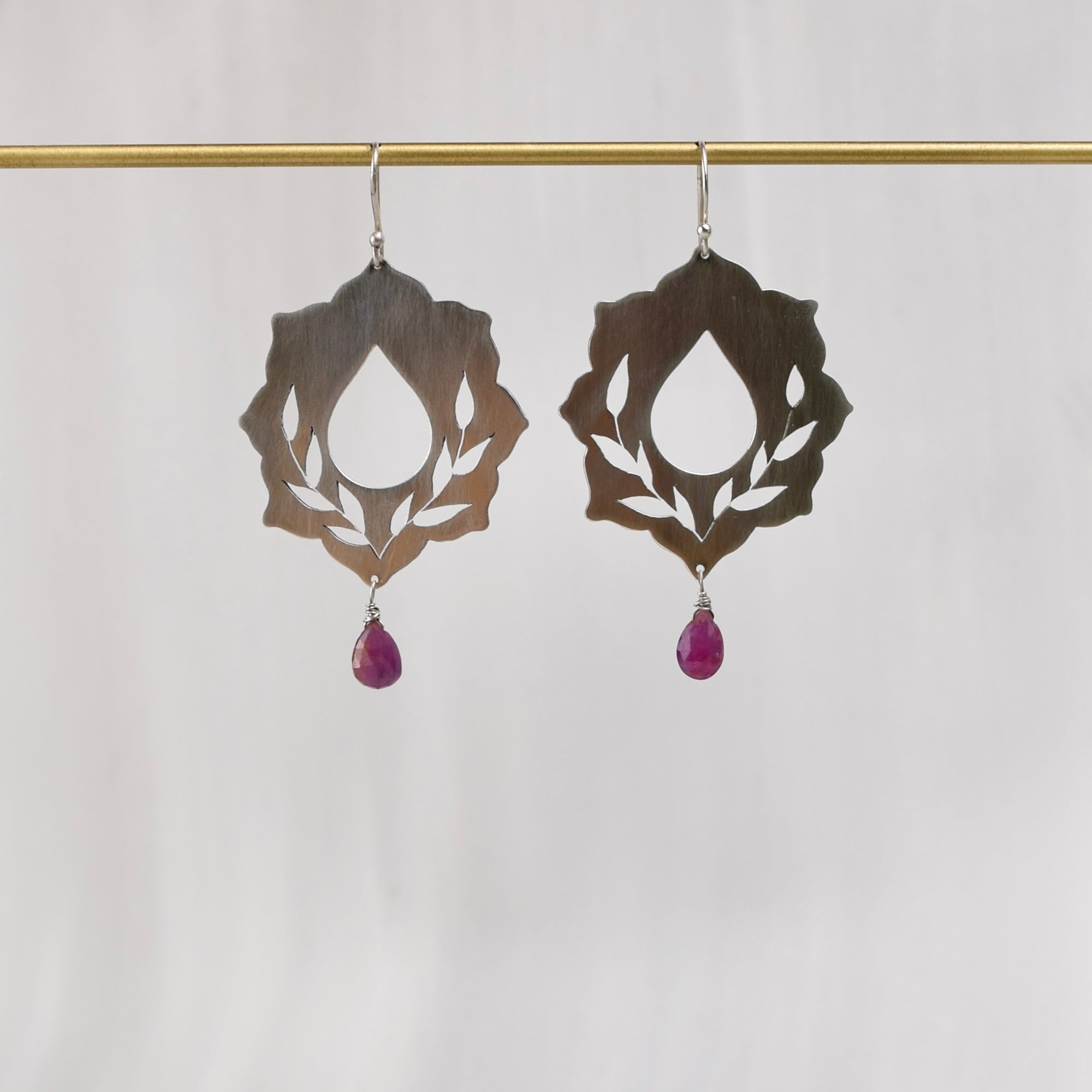 Ride with Me sterling silver pierced botanical dangle earrings with ruby droplet, hanging on brass display bar