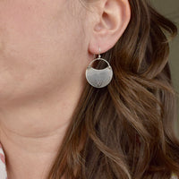 Model wearing medium handmade silver hydrangea crescent dangle earrings, rustic botanical jewelry handcrafted in Vermont